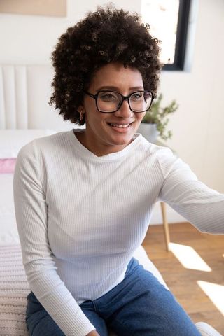Smiling Woman with Glasses Sitting on Bed in Natural Light