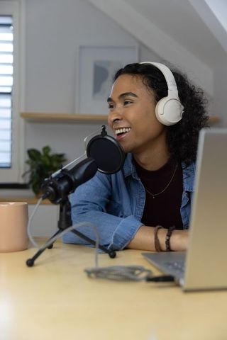 Hosting non-binary podcast in cozy loft studio with headphones microphone and laptop