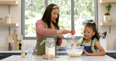 Parent and daughter baking together sifting flour at bright modern kitchen island