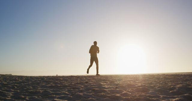 Person jogging along sandy beach during sunrise, seen in silhouette. Ideal for illustrating fitness, healthy lifestyle, outdoor activities, or early morning routines. Inspirational use for blogs, fitness programs, travel articles, and wellbeing promotions.