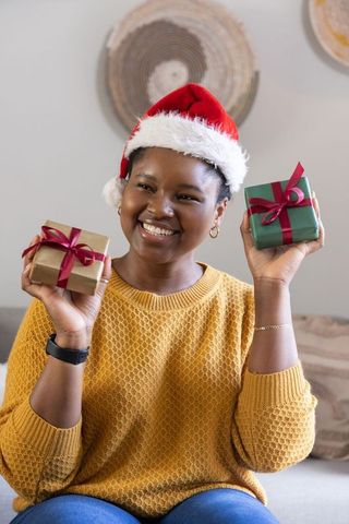 Smiling african american woman holding two wrapped holiday gifts wearing santa hat and cozy sweater