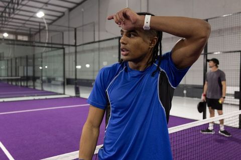 Tired player wiping forehead on purple indoor paddle court after intense rally