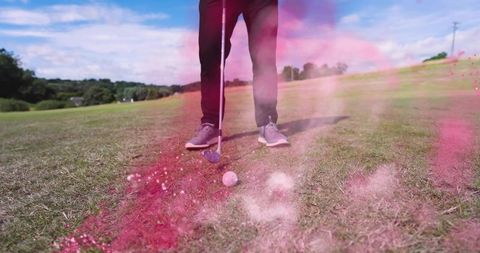 Golfer standing over ball on fairway holding club amid swirling pink smoke