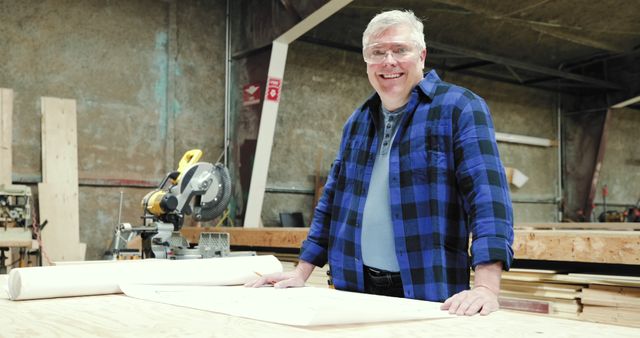 Smiling Woodworker in Workshop with Saw and Blueprints - Download Free Stock Images Pikwizard.com