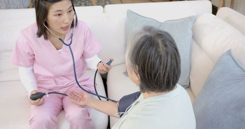 Nurse in pink scrubs checking blood pressure of senior at home