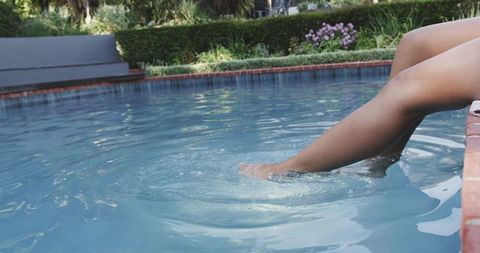 African american woman dipping foot in pool creating ripples on sunny poolside edge