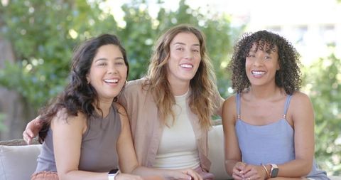 Diverse women laughing on backyard sofa showing watches and bracelets casual summer
