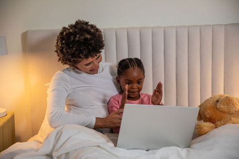Mother and daughter relaxing with laptop under cozy bedding