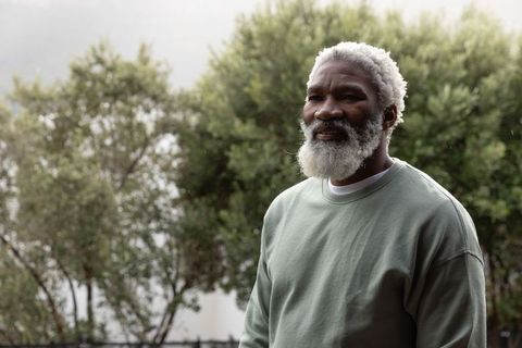 Senior african american man standing, gazing contemplatively in garden wearing sage crewneck