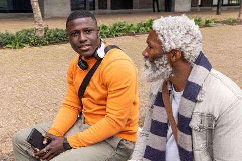 Intergenerational african american friends conversing on urban bench with smartphone