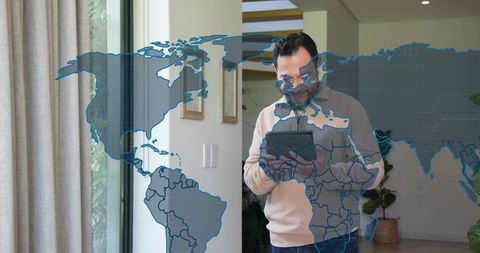 Mature asian man using tablet in contemporary home entry with translucent world map overlay