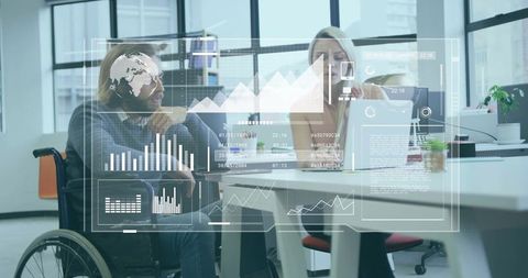 Collaborating wheelchair user and coworker analyzing digital dashboards in modern office