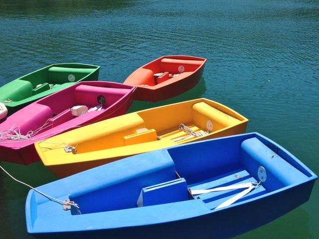 Several brightly colored rowboats gently float on calm lake waters, their vivid hues contrasting against the blue-green lake. Ideal for visuals related to outdoor activities, relaxation, summer vacations, and nature retreats.
