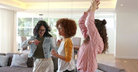 Multicultural friends dancing and laughing in bright modern living room with sofa