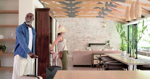 Diverse couple arriving at modern loft rental pulling luggage in sunlit living room