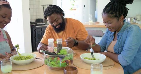 African family enjoying pesto pasta lunch with fresh salad in sunlit rustic kitchen