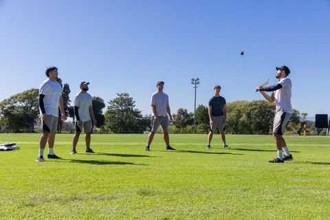 Friends playing casual baseball on sunny park field with batter swinging