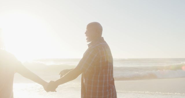 Couple holding hands, standing at beach, enjoying sunset. Good for travel promotions, romantic getaway advertisements, relationship articles, or summer vacation concepts.