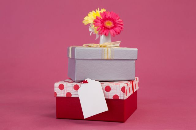 Stack of gift boxes with tag and flowers on pink background