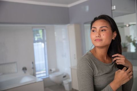 Asian Woman in Her 30s Styling Hair in Modern Minimalist Bathroom