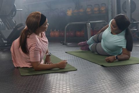 African american women performing plank exercises together on green mats in modern gym