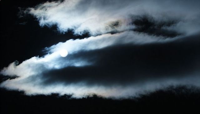 Gibbous Moon Slipping Behind Luminous Cloud Bands Creating Halo and Moody Night Sky