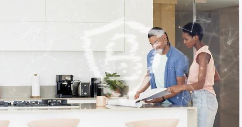 Couple reviewing home blueprint in modern kitchen with digital network overlay