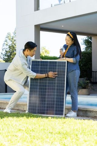 Asian couple installing solar panel by backyard pool enjoying sustainable home upgrade