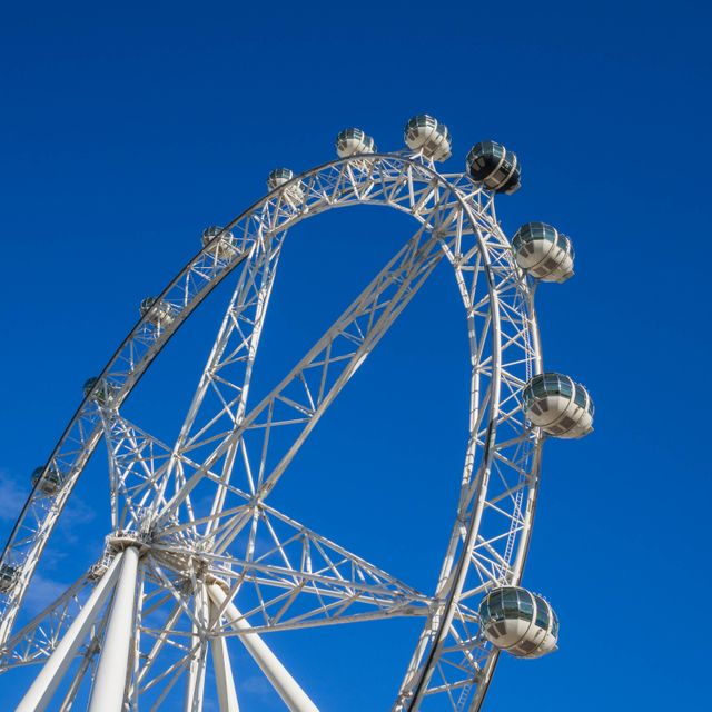 Close-up of large ferris wheel against a vivid blue sky, highlighting the engineering marvel and its individual cabins. Ideal for promoting tourism, travel destinations, amusement parks, or engineering marvels.