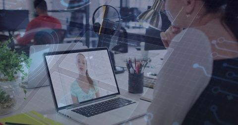 Woman watching virtual presentation on laptop in open office with digital overlays for remote work