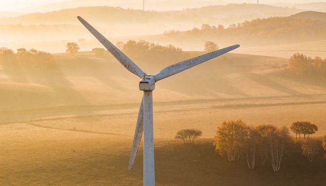 Towering wind turbine bathing misty rolling hills in warm golden hour light