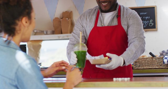 African american man wearing apron serving and fries smoothie to a woman at the food truck. food truck and street food concept