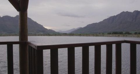 Wooden gazebo railing framing tranquil mountain lake under overcast sky for lakeside retreat