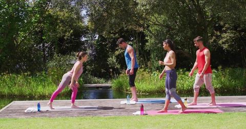 People practicing yoga outdoors on deck by pond in sunlit park