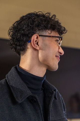 Curly-haired young man wearing tortoiseshell glasses and turtleneck overcoat, side profile
