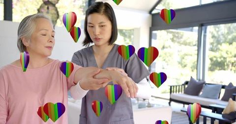 Home caregiver guiding senior through arm rehabilitation with rainbow heart support