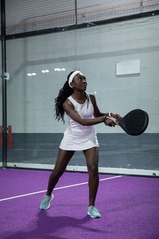 African american woman playing padel on purple court holding paddle preparing shot