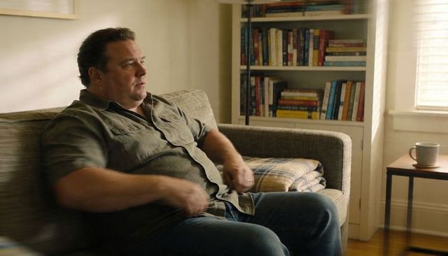 Middle-aged man sitting on couch in cozy living room with bookshelf and coffee mug