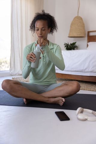 African american woman sitting cross-legged removing water bottle cap after home workout