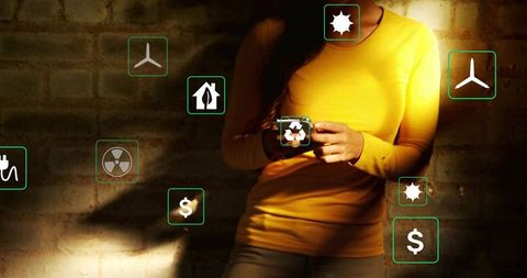 Woman tapping smartphone showing renewable energy and finance icons on brick wall