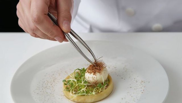 Chef placing crispy garnish with tweezers on plated starter with microgreens and mousse