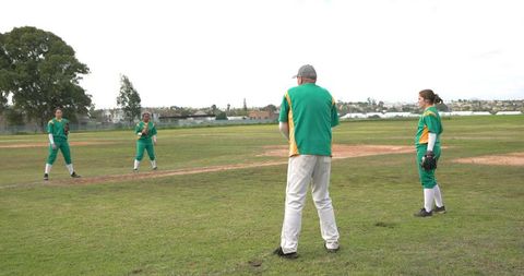 Senior male coach and female softball team practicing fielding outdoors