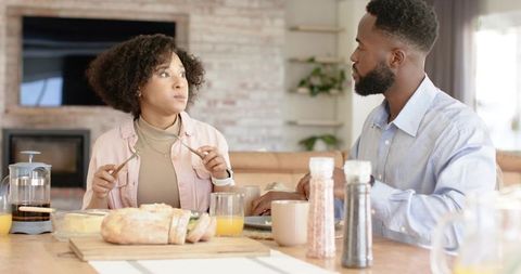 Mid-Adult Couple Having Breakfast at Sunlit Wooden Table, Engaged Conversation