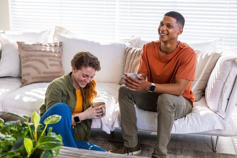 Young couple laughing and sipping coffee on bright white sofa in sunlit living room