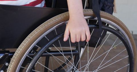 Wheelchair user gripping push rim on brick pavement closeup showing mobility and independence