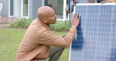 Mature technician inspecting solar panel with team during residential installation