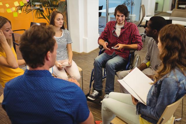 Colleagues sitting in a circle and engaging in discussion in a modern office environment. Use this image to represent collaboration, diversity, teamwork, business meetings, and inclusive workspaces.