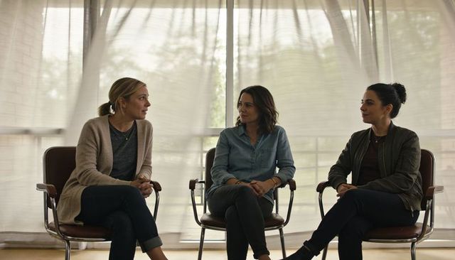 Three women sharing supportive conversation in sunlit meeting space, casual clothes