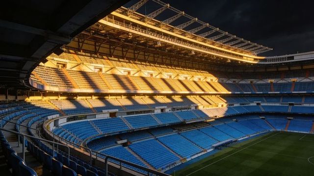 Empty football stadium bowl glowing with golden sunlight over tiered blue seats at dusk