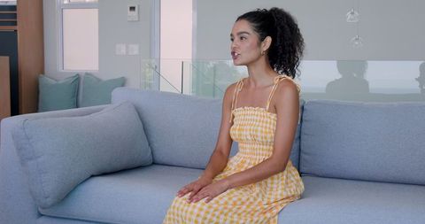Young Woman Sitting on Sofa Indoors Wearing Yellow Checkered Dress